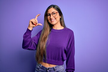 Wall Mural - Young beautiful smart woman wearing glasses over purple isolated background smiling and confident gesturing with hand doing small size sign with fingers looking and the camera. Measure concept.