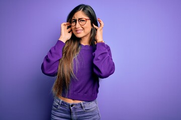 Wall Mural - Young beautiful smart woman wearing glasses over purple isolated background covering ears with fingers with annoyed expression for the noise of loud music. Deaf concept.