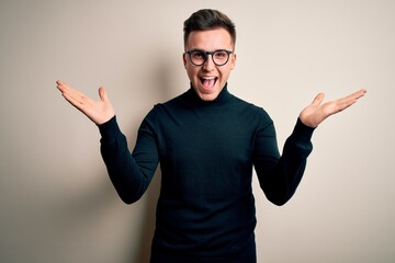 Wall Mural - Young handsome caucasian man wearing glasses and casual sweater over isolated background celebrating crazy and amazed for success with arms raised and open eyes screaming excited. Winner concept