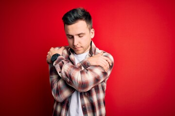 Wall Mural - Young handsome caucasian man wearing casual modern shirt over red isolated background Hugging oneself happy and positive, smiling confident. Self love and self care