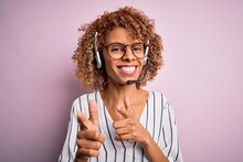African American Curly Call Center Agent Woman Working Using Headset Over Pink Background Pointing Fingers To Camera With Happy And Funny Face. Good Energy And Vibes.