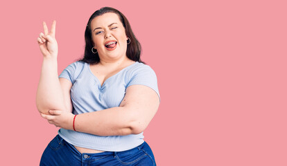 Young plus size woman wearing casual clothes smiling with happy face winking at the camera doing victory sign. number two.