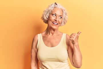 Wall Mural - Senior grey-haired woman wearing casual clothes smiling with happy face looking and pointing to the side with thumb up.