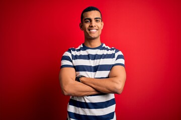 Wall Mural - Handsome african american man wearing casual striped t-shirt standing over red background happy face smiling with crossed arms looking at the camera. Positive person.