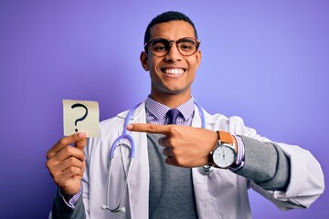 Wall Mural - Handsome african american doctor man wearing stethoscope holding question mark reminder very happy pointing with hand and finger