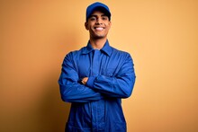 Young African American Mechanic Man Wearing Blue Uniform And Cap Over Yellow Background Happy Face Smiling With Crossed Arms Looking At The Camera. Positive Person.