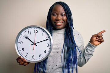 Sticker - Young african american plus size woman with braids doing countdown holding big clock very happy pointing with hand and finger to the side