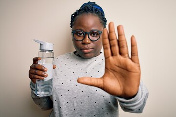 Poster - Young african american plus size sportswoman with braids drinking bottle of water with open hand doing stop sign with serious and confident expression, defense gesture