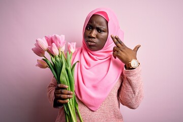 Poster - Young african american plus size woman wearing muslim hijab holding bouquet of pink tulips Shooting and killing oneself pointing hand and fingers to head like gun, suicide gesture.