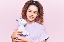 Beautiful Kid Girl With Curly Hair Holding Animal Doll Toy Looking Positive And Happy Standing And Smiling With A Confident Smile Showing Teeth
