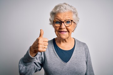 Wall Mural - Senior beautiful grey-haired woman wearing casual sweater and glasses over white background doing happy thumbs up gesture with hand. Approving expression looking at the camera showing success.