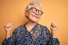 Senior Beautiful Grey-haired Woman Wearing Casual Shirt And Glasses Over Yellow Background Very Happy And Excited Doing Winner Gesture With Arms Raised, Smiling And Screaming For Success. Celebration.