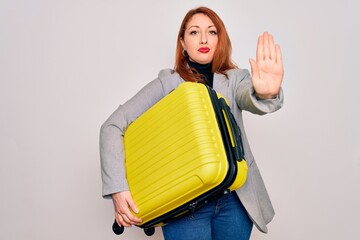 Poster - Young beautiful redhead woman holding suitcase prepared to business travel with open hand doing stop sign with serious and confident expression, defense gesture