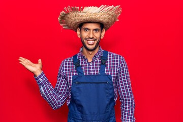 Sticker - Young latin man wearing farmer hat and apron smiling cheerful presenting and pointing with palm of hand looking at the camera.