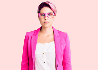 Canvas Print - Young beautiful woman with pink hair wearing business jacket and glasses with serious expression on face. simple and natural looking at the camera.