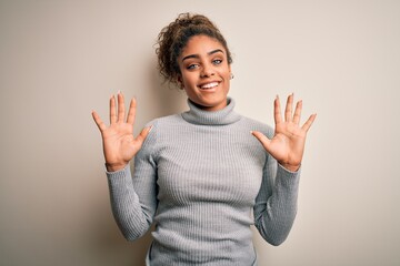 Sticker - Beautiful african american girl wearing turtleneck sweater standing over white background showing and pointing up with fingers number ten while smiling confident and happy.