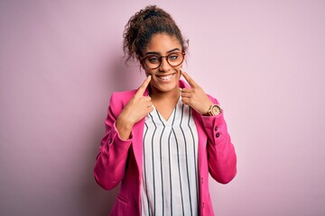 Wall Mural - Beautiful african american businesswoman wearing jacket and glasses over pink background Smiling with open mouth, fingers pointing and forcing cheerful smile