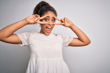 Poster - Young beautiful african american girl wearing casual t-shirt standing over white background Doing peace symbol with fingers over face, smiling cheerful showing victory