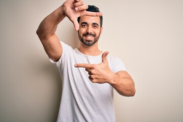 Canvas Print - Young handsome man with beard wearing casual t-shirt standing over white background smiling making frame with hands and fingers with happy face. Creativity and photography concept.