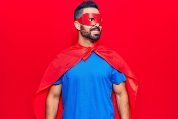 Poster - Young hispanic man wearing super hero costume looking to side, relax profile pose with natural face and confident smile.