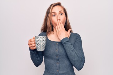 Wall Mural - Young beautiful blonde woman drinking a cup of coffee covering mouth with hand, shocked and afraid for mistake. surprised expression