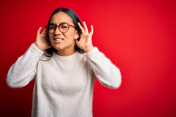 Poster - Young beautiful asian woman wearing casual sweater and glasses over red background Trying to hear both hands on ear gesture, curious for gossip. Hearing problem, deaf