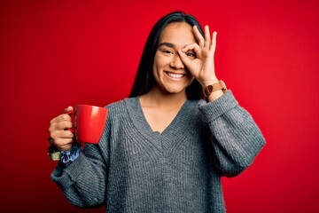 Canvas Print - Young beautiful asian woman drinking mug of coffee standing over isolated red background with happy face smiling doing ok sign with hand on eye looking through fingers