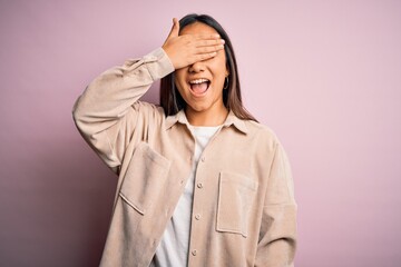 Sticker - Young beautiful asian woman wearing casual shirt standing over pink background smiling and laughing with hand on face covering eyes for surprise. Blind concept.