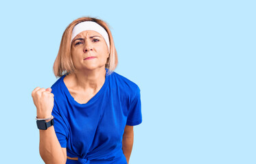 Poster - Young blonde woman wearing sportswear angry and mad raising fist frustrated and furious while shouting with anger. rage and aggressive concept.