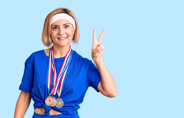 Poster - Young blonde woman wearing winner medals smiling with happy face winking at the camera doing victory sign. number two.