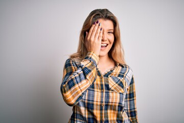 Canvas Print - Young beautiful blonde woman wearing casual shirt standing over isolated white background covering one eye with hand, confident smile on face and surprise emotion.