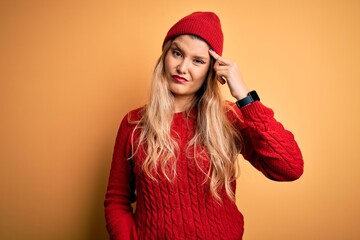 Poster - Young beautiful blonde woman wearing casual sweater and wool cap over white background pointing unhappy to pimple on forehead, ugly infection of blackhead. Acne and skin problem