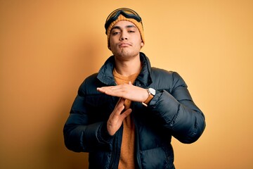 Wall Mural - Young brazilian skier man wearing snow sportswear and ski goggles over yellow background Doing time out gesture with hands, frustrated and serious face