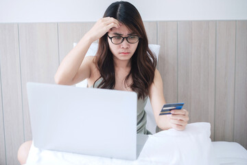 Happy woman holding credit card and using computer laptop for online shopping while making orders on bed in morning at home. Business, technology, ecommerce, digital banking and online payment concept