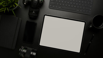 Blank screen tablet on dark modern workspace with digital devices, supplies and decoration