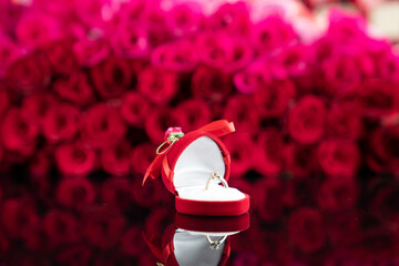 Romantic day concept. Wedding rings lying on shining table on the red roses background. 