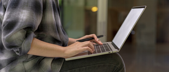 Female worker sitting on table while working with mock-up laptop in comfortable office room