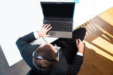 Poster - Top view of a man at a laptop. Remote communication. Communication via the Internet. A person with headphones and a microphone communicates online.