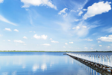 Wall Mural - Blue sky with light clouds, blue water and white pier in the sunny summer day.