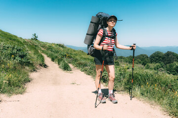 woman hiker on summer day in shorts and with big heavy hiking backpack and chopsticks. the local tra