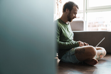 Photo of redhead man working with laptop while sitting on floor