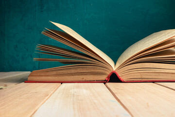 Poster - Beautiful ancient open old book on a red  wooden table and dark-green wall background behind.
