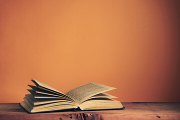 Poster - Old  open book on a oak wooden table. Background of orange wall behind.