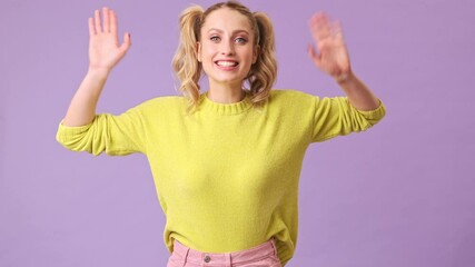 Wall Mural - A beautiful blonde with a smile sways in different directions, friendly waves his hands in an isolated studio on a purple background