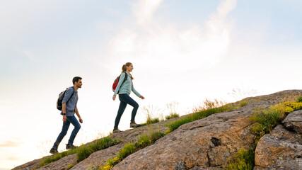 Wall Mural - couple of young happy travelers hiking with backpacks on the rocky trail at the evening. family trav