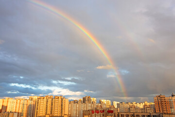 Wall Mural - Bright colorful rainbow over, sun shining in rainy day, beautiful colors phenomenon sky weather, multi-storey residential buildings, summer season.