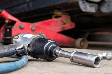 Pneumatic wrench tool on the asphalt and a car jack for lift up the body and changing the tire. Car without wheel