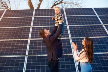 young man throws up a small child on a background of solar panels under a blue sky. a beautiful woma