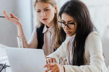 Poster - selective focus of businesswoman in glasses looking at laptop near coworker