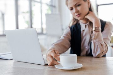 Poster - selective focus of businesswoman touching cup of coffee near laptop